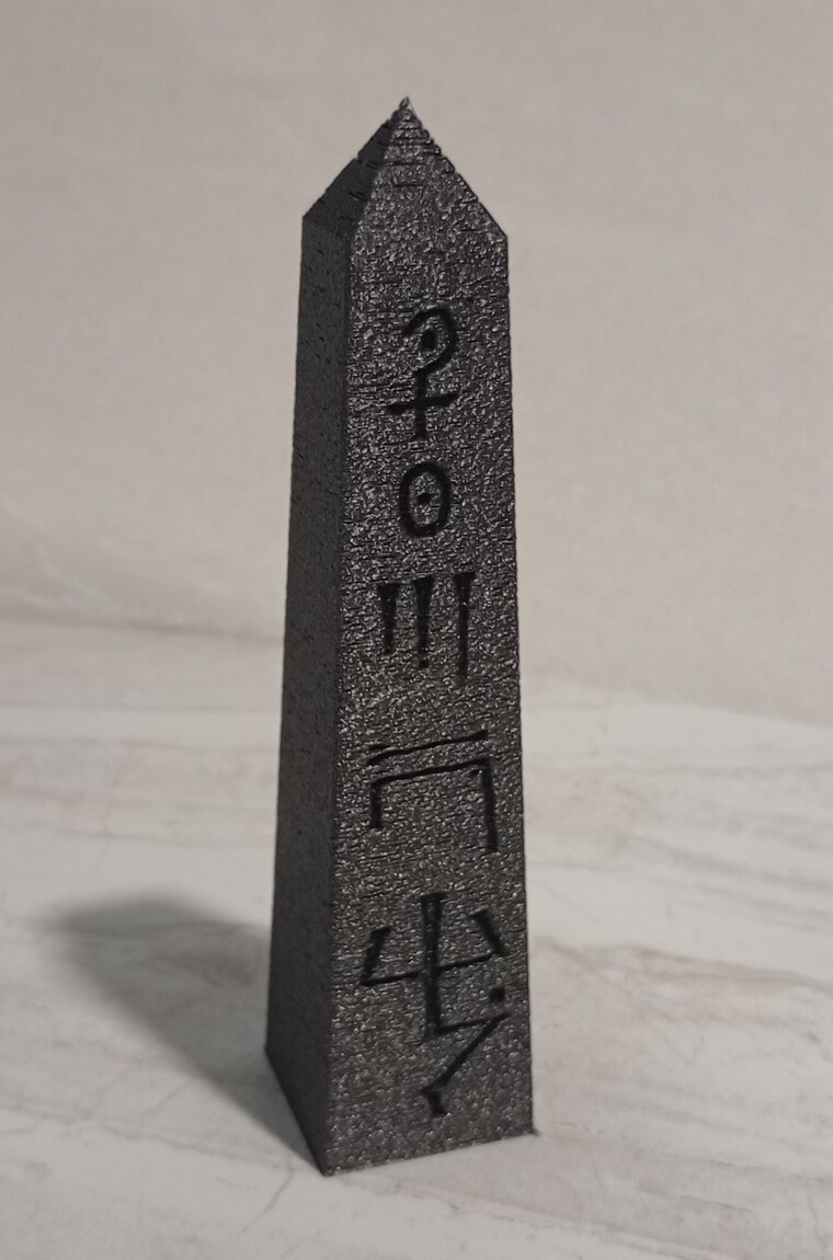 the same obelisk printed in galaxy black PLA, glyphs legible in the surface